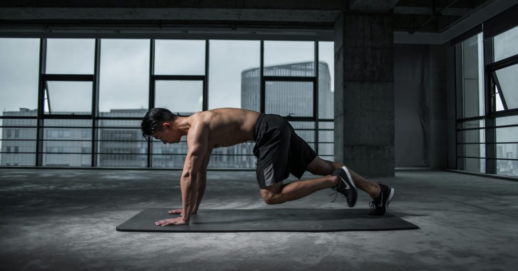 Man doing mountain climbers on a mat in a gym with cityscape in the background